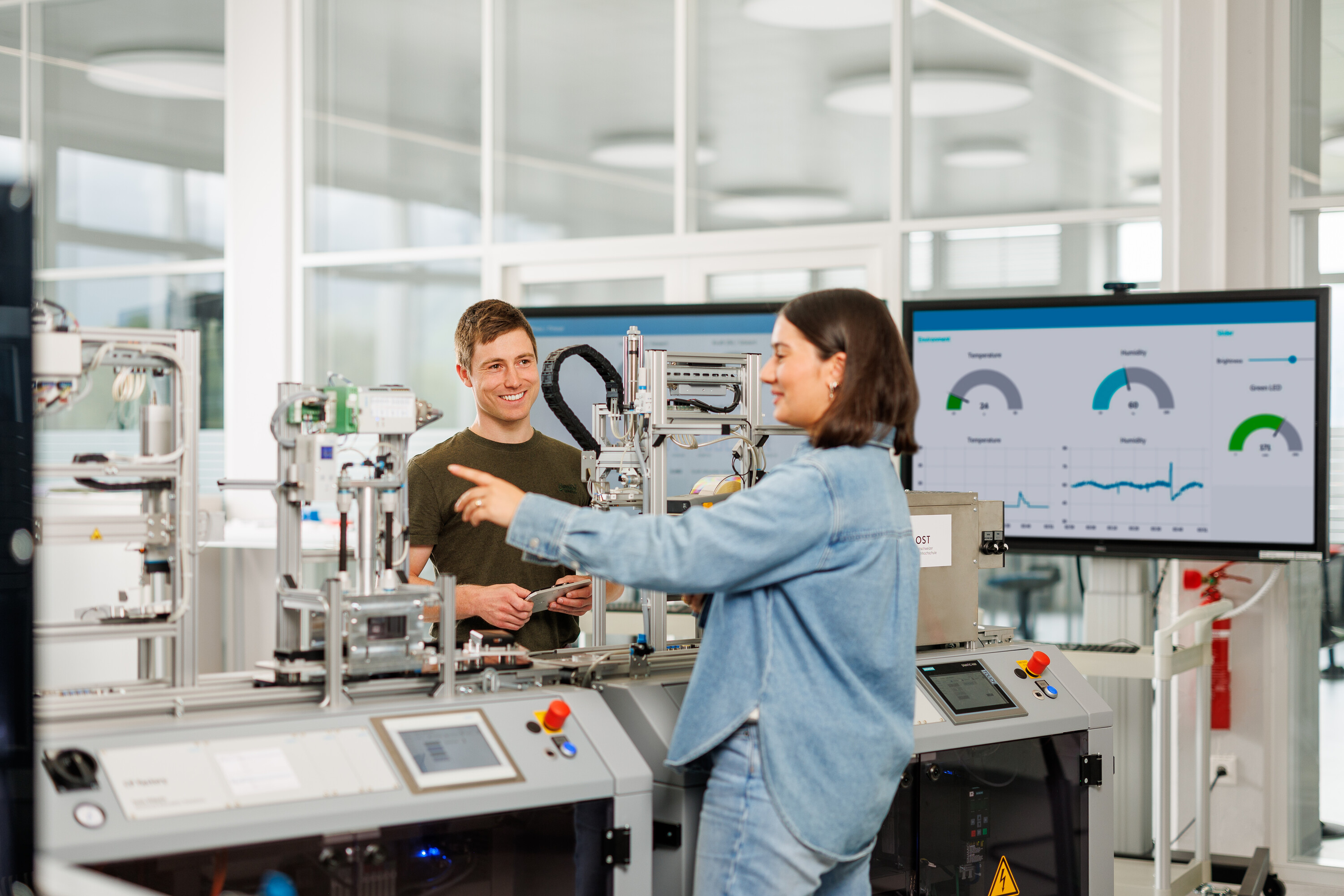 Zwei Studierende der Mechatronik arbeiten an einer Maschinenanlage in der smarten Fabrik der OST.