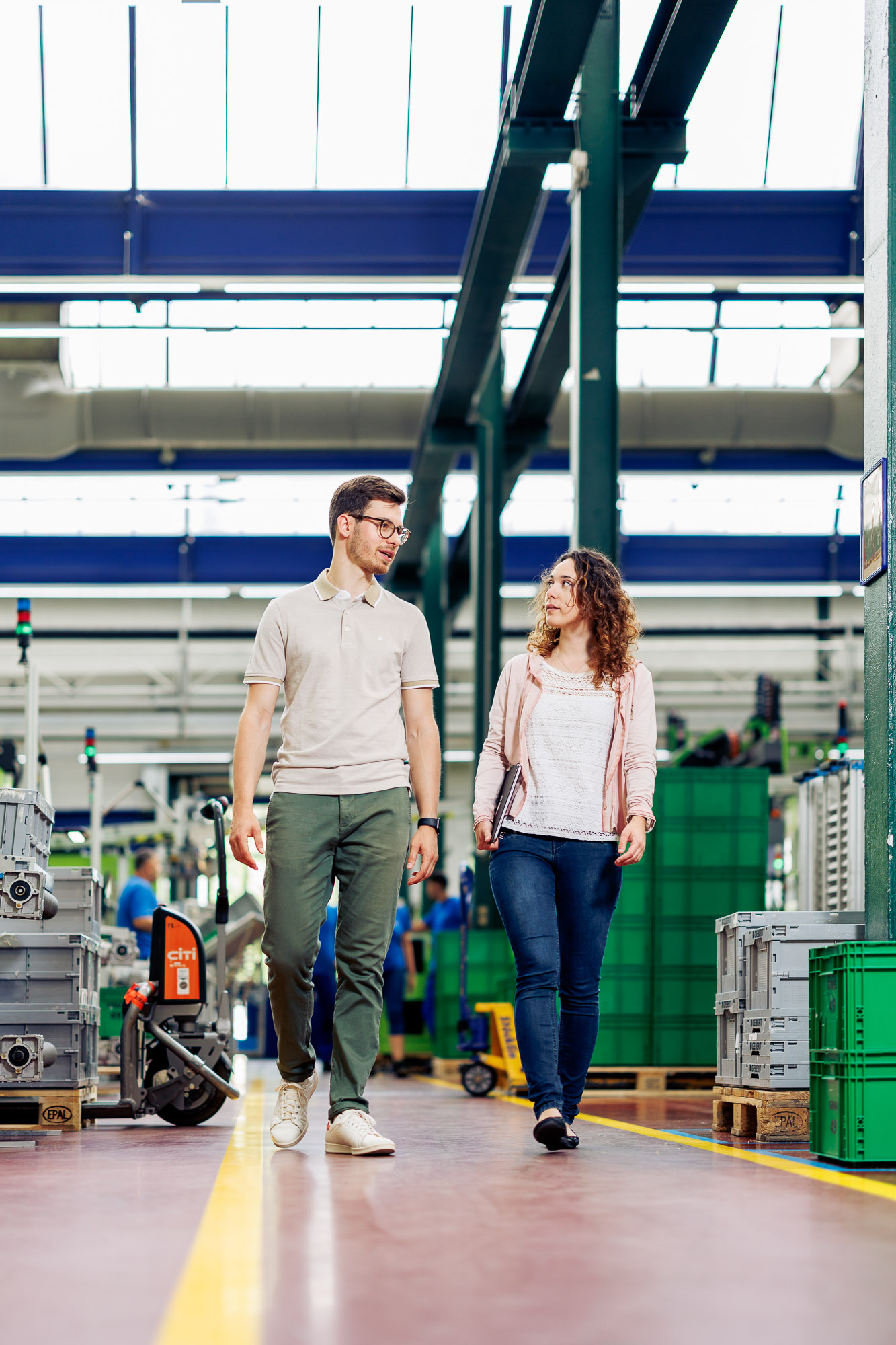 Eine angehende Wirtschaftsingenieurin und ein angehender Wirtschaftsingenieur unterhalten sich in einer Lagerhalle.